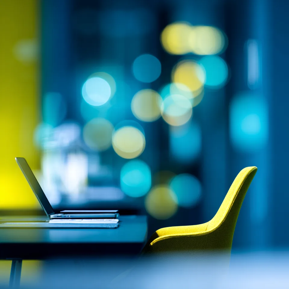 Laptop and a yellow chair at a workspace in front of blurred blue lights