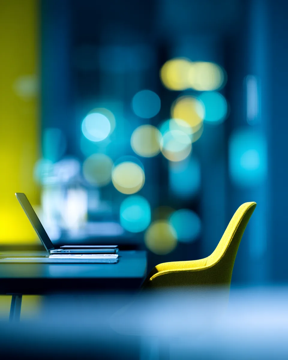 Laptop and a yellow chair at a workspace in front of blurred blue lights